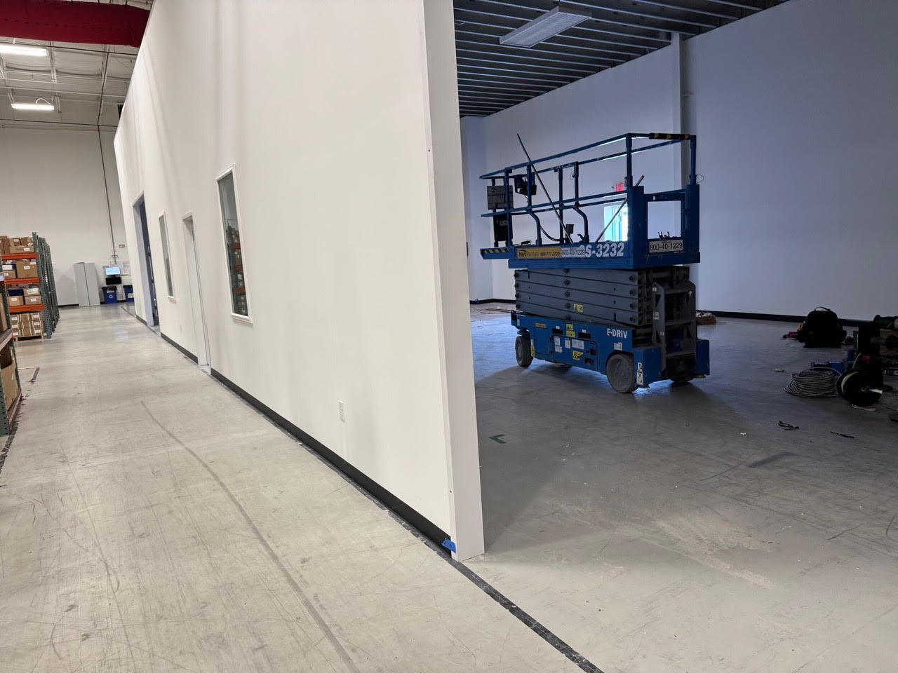 A long finished corridor wall in the Teknoware building with interior windows and a scissor lift at the far end