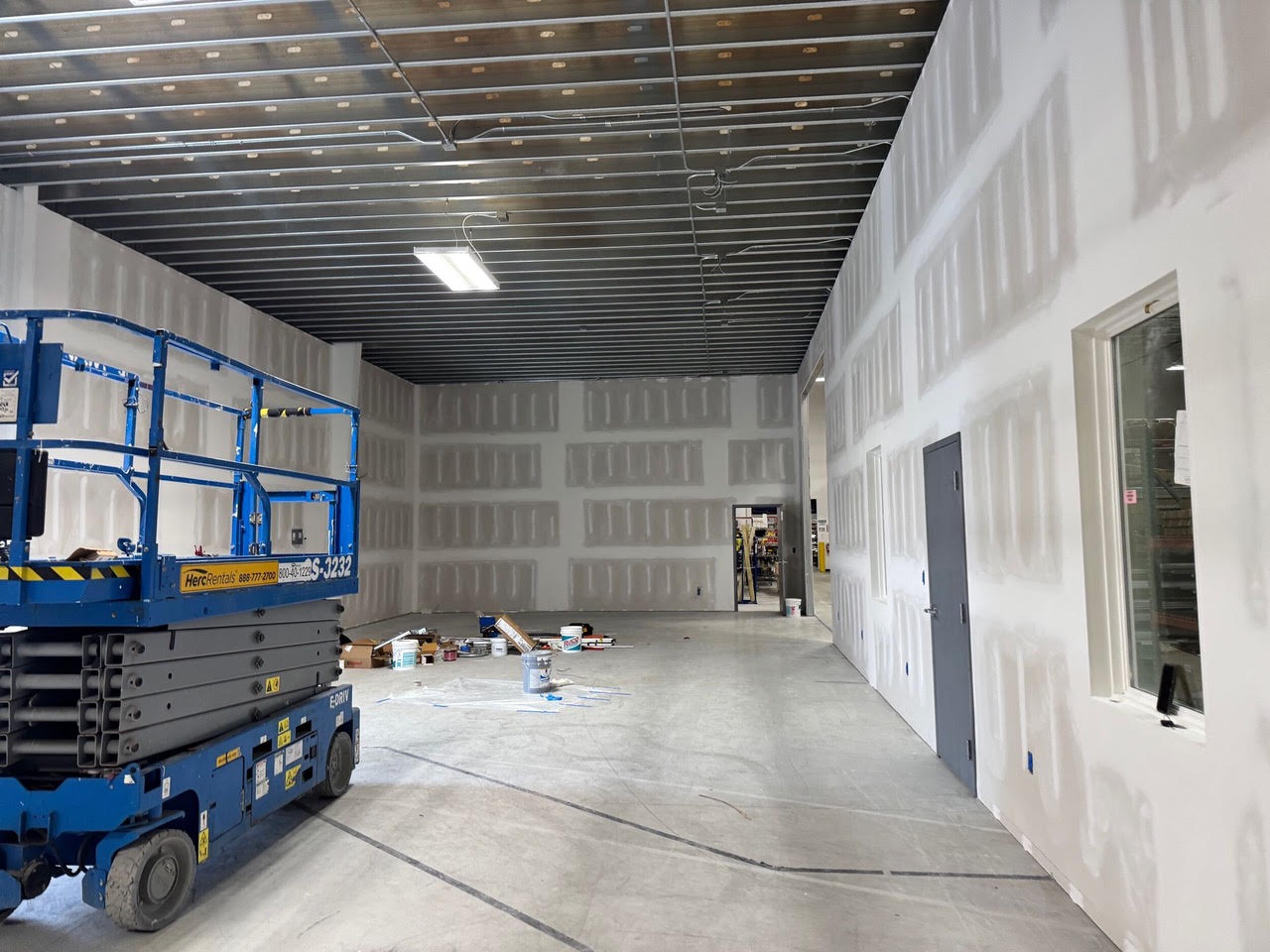A new office space at Teknoware with taped drywall, an interior window and a door, and a scissor lift in the room