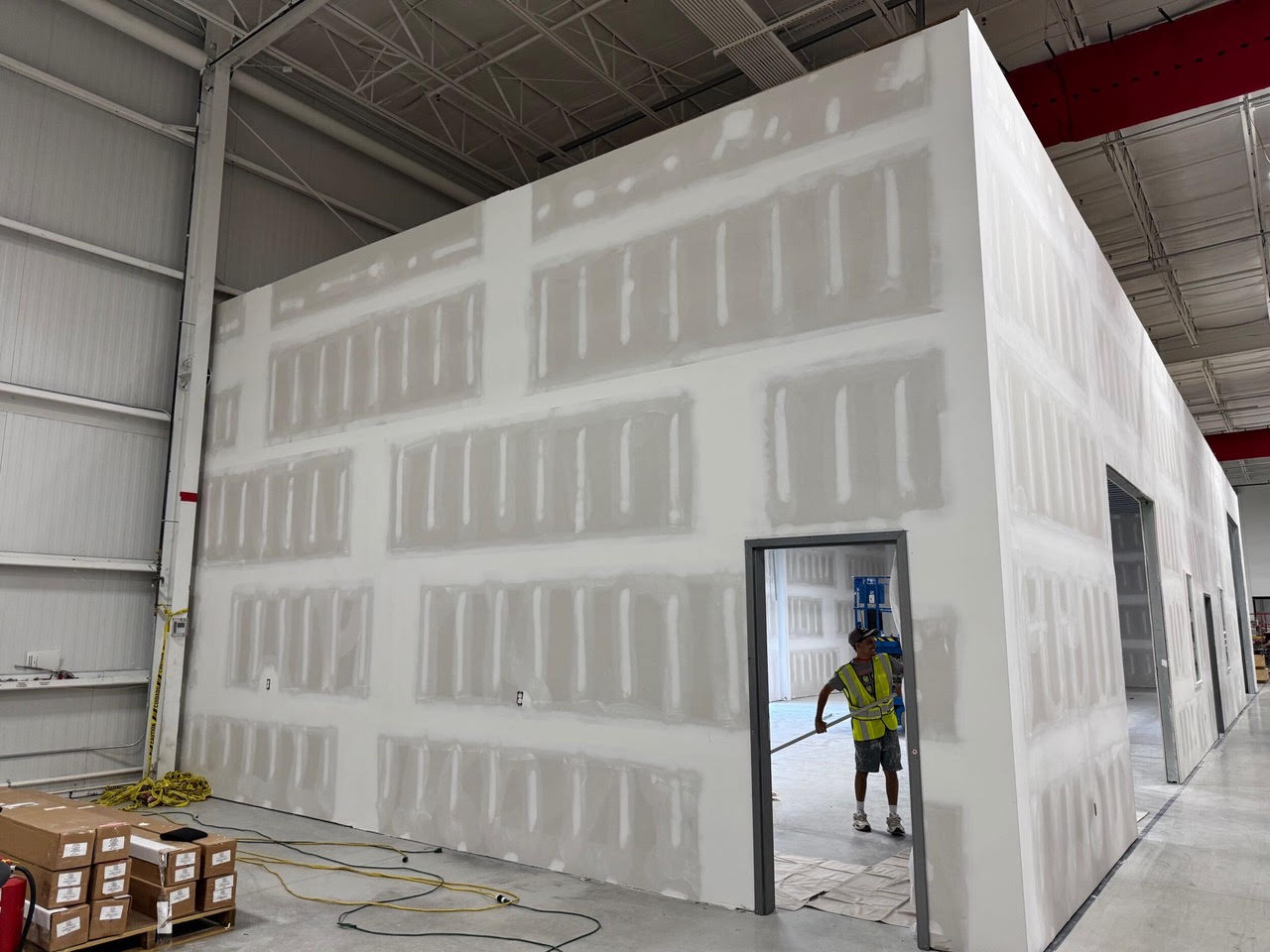 New taped walls rising inside the Teknoware warehouse, with a crew member in the doorway