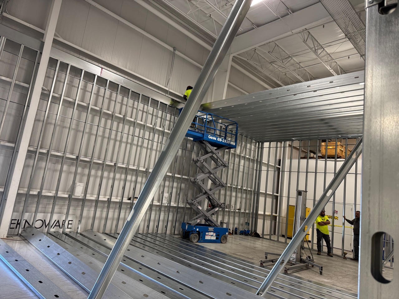 Metal stud framing for the new Teknoware space, with the Teknoware name on the floor and a scissor lift beyond